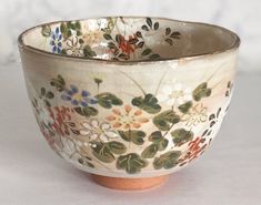 a bowl with flowers painted on it sitting on a white table top next to a wall