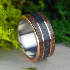 a wedding ring made out of wood and copper in front of some green plants on a table