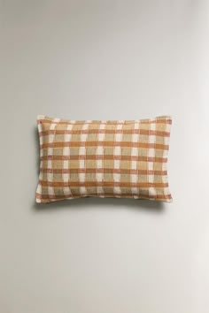 an orange and white checkered pillow on a gray wall