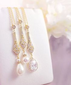 three necklaces with pearls and diamonds on a white piece of cloth next to flowers