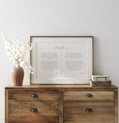 a wooden dresser topped with drawers and a vase filled with flowers next to a framed poem