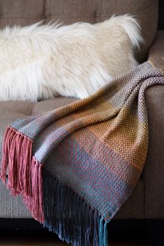 a dog laying on top of a couch next to a blanket and pillow with fringes