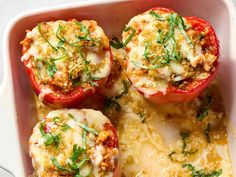 four stuffed red peppers in a casserole dish with cheese and herbs on top