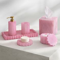 pink bathroom accessories on white surface with gold accents and soap dispenser in center