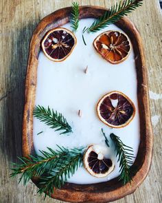 orange slices are arranged on top of milk in a wooden tray with greenery and pine needles