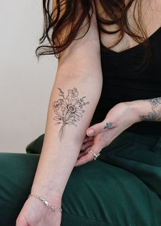 a woman with tattoos on her arm and wrist holding a flower in her left hand