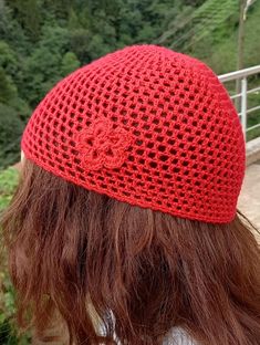 a woman wearing a red crocheted hat with a flower on the front and side