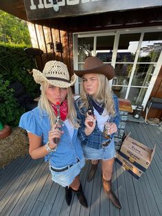 two women in cowboy hats are standing on a porch holding wine glasses and looking at the camera