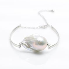 a white bracelet with a pearl on the end and silver chain around it, sitting on a white surface