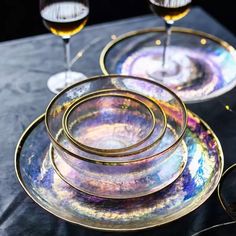 three wine glasses sitting on top of plates with gold rims and saucers in front of them