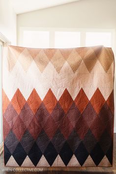 an orange, brown and black quilt sitting on top of a wooden floor next to a window