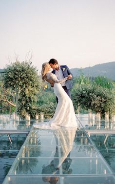 a bride and groom kissing in front of an outdoor ceremony venue with clear glass flooring