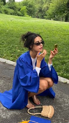 a woman sitting on the ground taking a photo with her cell phone wearing a blue graduation gown