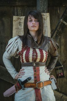 a woman dressed as a pirate standing in front of a wooden wall with her hands on her hips