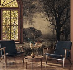 two chairs and a table in front of a window with a painting on the wall