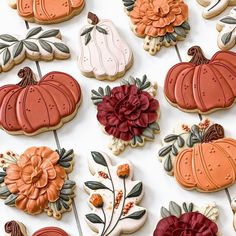 many decorated cookies are arranged on a white surface with flowers and pumpkins in the background