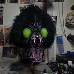 a monster mask with green eyes and fangs on it's head in a messy room