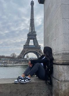 a woman sitting on the edge of a wall next to the eiffel tower