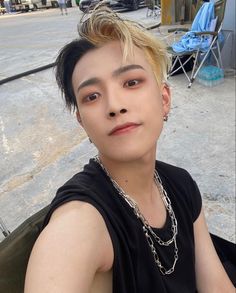 a young man sitting on the ground wearing a black shirt and silver chains around his neck