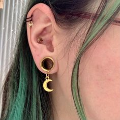 a close up of a person wearing earring with green hair and piercings on their ears