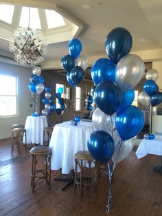 blue and silver balloons are in the middle of a room with white tablecloths