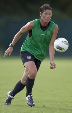 a woman in a green shirt is playing soccer on the field with a white ball