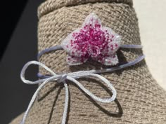 a close up of a hat with a pink flower on the front and white ribbon around it