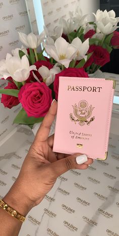 a person holding a pink passport next to flowers