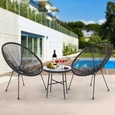 two wicker chairs and a table with wine on it in front of a swimming pool