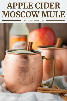 an apple cider moscow mule with cinnamon sticks in it and two glasses filled with the same drink