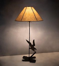 a lamp with a bird on it sitting on top of a table next to a wall