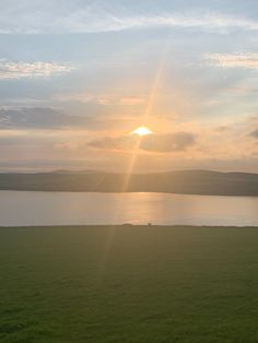 the sun is setting over a large body of water with green grass in front of it