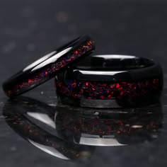 two black wedding bands with red and blue glitter inlays, on a reflective surface