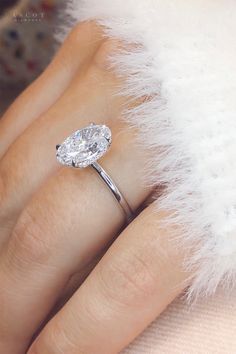 a woman's hand with a diamond ring on top of her finger and white fur