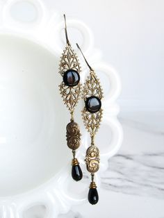 These dangle earrings are made with vintage glass black stones, black Czech glass beads, and brilliantly detailed brass filigree. The ear wires are antiqued brass. The earrings are 3.5" long from the top of the ear wires to the bottom of the dangles. Without the ear wires, they are 2.75" long.  ------------------- **Please be sure to read my shipping and store policies, and don't hesitate to send me a message with any questions you may have! INTERNATIONAL BUYERS: Please be aware that there may be taxes or customs fees that are not included in the purchase price. I cannot reimburse for additional fees. Vintage Black Jewelry With Antique Finish, Vintage Black Dangle Jewelry, Vintage Bronze Chandelier Earrings In Brass, Vintage Brass Filigree Chandelier Earrings, Black Czech Glass Jewelry With Ear Wire, Elegant Black Czech Glass Earrings, Elegant Black Jewelry With Antique Finish, Vintage Bronze Brass Chandelier Earrings, Black Filigree Dangle Jewelry