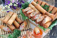 there are many rolls on the table with dipping sauces and flowers in the background