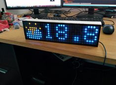 an electronic clock sitting on top of a desk next to a computer monitor and keyboard