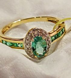 This ring features: * 1 x oval cut Zambian emerald gem measuring approx 6x4mm with a minimum gemstone weight of 0.39ct. * 8 x round cut Zambian emerald gems measuring approx 2mm with a minimum gemstone weight of 0.23ct. * 16 x round cut diamonds measuring approx 1mm with a minimum gemstone weight of 0.08ct. * The total weight for this piece is 0.73ct. * The ring sits approx 5mm above the finger and measures approx 9mm down the finger. * The band measures approx 3mm at the shoulder and tapers to Oval Yellow Gold Emerald Ring With Halo, Oval Halo Emerald Ring For May Birthstone, Halo Oval Diamond Ring For May Birthstone, Oval Emerald Ring With Halo Design, Oval Emerald Ring With Halo For Promise, Oval Diamond Ring With Halo For May Birthstone, Green Oval Diamond Ring With Center Stone, Green Oval Birthstone Ring For Anniversary, Oval Emerald Birthstone Ring With Halo Setting