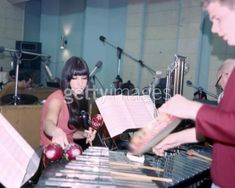 two people are playing music in a recording studio, one is holding an instrument and the other is looking at records