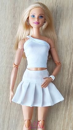 a barbie doll wearing a white dress and sandals on top of a wooden floor next to a wall