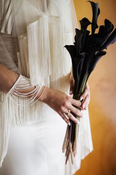 a woman in a white dress holding a bouquet of black calla lilies with her hands