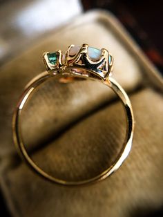 One of the most stunning and unique rings that we have had in the shop to date! Featuring two oval cut cabochon Australian Opals in a moi et toi setting, it is further enhanced by two round cut emerald stones and set in hallmarked 9ct yellow gold. Size: UK I 1/2 // US 5 // EUR 48 (sizeable for an additional fee) Gemstone: Australian Opal and Emerald Metal: 9ct (9k) Hallmarked Yellow Gold Ring Face Dimensions: 10mm wide x 9mm tall x 4mm rise Band Dimensions: 1.25mm Maker: Unknown (Mark GJL or CJL Emerald Opal Ring, Emerald And Opal Ring, Trillion Cut Ring, Antique Opal Ring, Face Dimensions, Amethyst Ring Vintage, Graduation Rings, Emerald Stone, Opal Ring