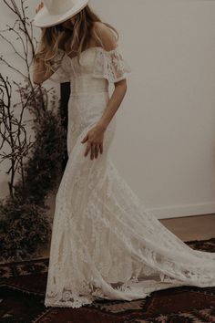 a woman in a white dress and hat standing next to a plant wearing a straw hat