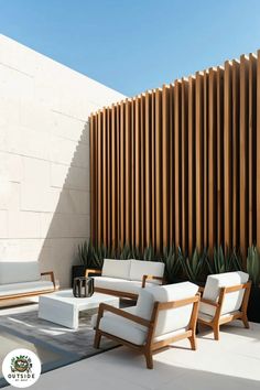 an outdoor living area with white furniture and wood slats on the wall behind it