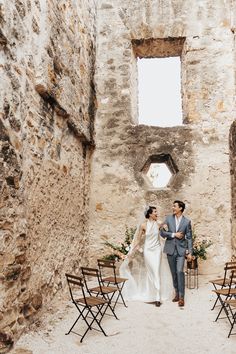 a bride and groom walking through an old stone building with chairs in the foreground