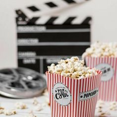 three red and white striped popcorn buckets next to a movie clapper on a table