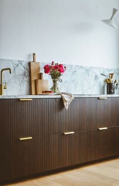 a kitchen with marble counter tops and wooden cabinets, flowers in vases on the island