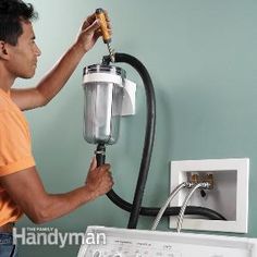 a man using a blow dryer on the wall to clean his clothes in front of an appliance