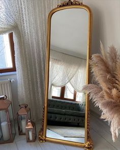 a large mirror sitting on top of a white floor next to a vase filled with dry grass