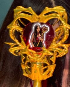 a woman with long hair wearing a gold mask and holding a heart shaped object in her hand